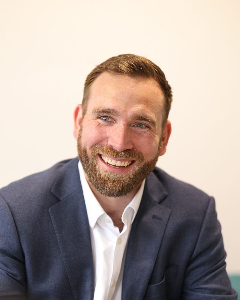 Andrew Marcinko laughing, in a navy blazer and white shirt